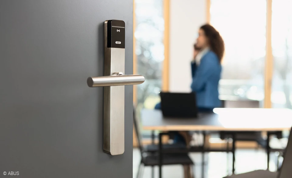 Im Vordergrund eine moderne Bürotür mit TECTIQ-Beschlag. Im Hintergrund eine telefonierende Frau.